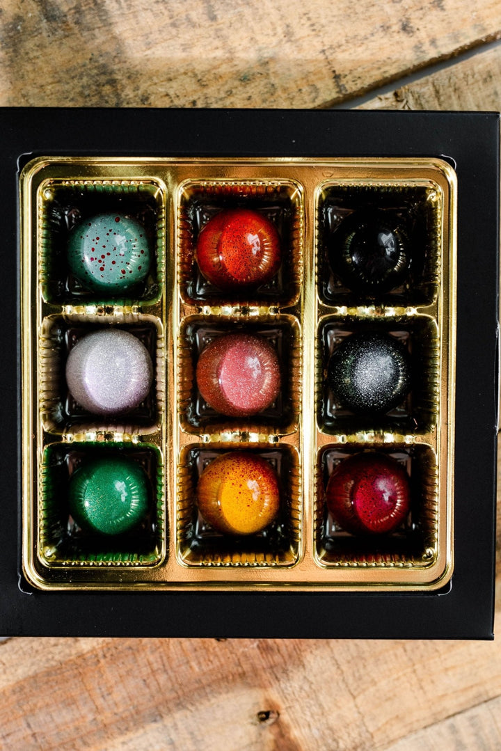 Hill Country Chocolate’s 9 Piece Signature Artisanal Bonbons feature glossy, colorful spheres in a gold tray inside a black box—an ideal handmade treat for chocolate lovers.