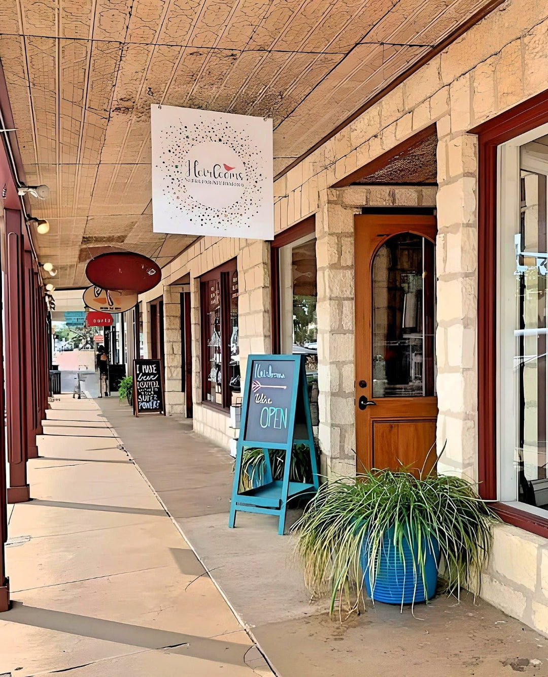 Heirlooms store exterior with rustic stone walls, wooden door, blue welcome sign, and green plant in a blue pot