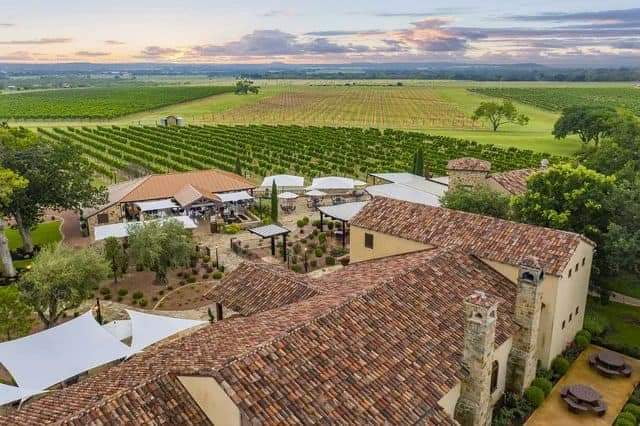 Vineyard estate with terracotta roof, outdoor seating, and scenic Texas hill country views at sunset