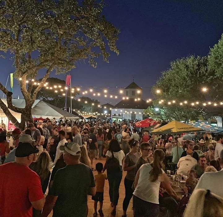 Outdoor Fredericksburg community festival at night with string lights, vendor tents, and lively crowd