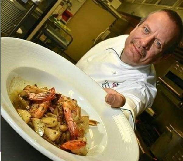 Chef presenting shrimp and roasted potato dish in white bowl, gourmet plating, kitchen background