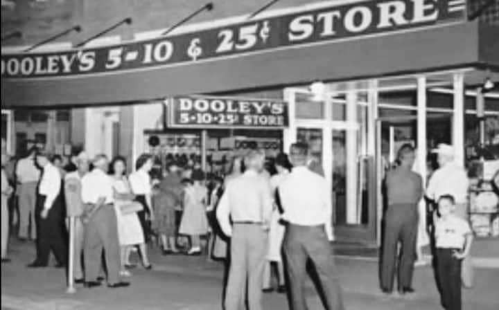Vintage black-and-white photo of Dooley's 5-10 & 25¢ Store exterior with marquee sign, metallic storefront, and crowd, highlighting historic shopping experience.