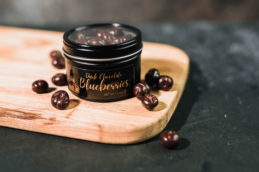 Dark Chocolate Blueberries in a black jar with glossy chocolate coating, displayed on a wooden board