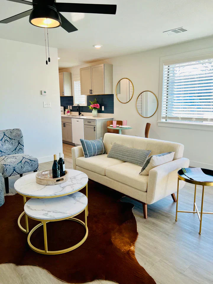 Modern cream loveseat with wood legs, marble-top nesting tables, and cowhide rug in a bright living room, vendor-supplied, perfect for Fredericksburg Texas Store shoppers.