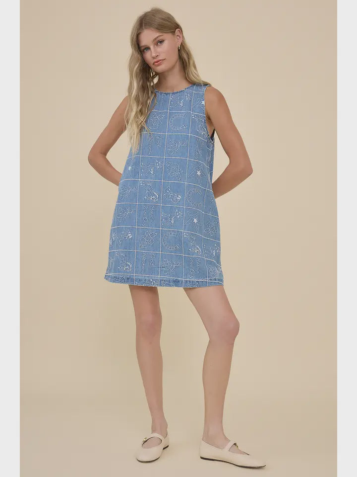 A woman with long blonde hair wears the Zertz EMBROIDERED DENIM WESTERN DRESS and beige flats, standing against a plain beige background with one leg slightly bent.