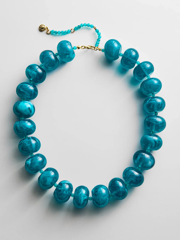 The Zertz JOAN SEMI PRECIOUS NECKLACE features large, round, translucent turquoise beads, a gold clasp, and small turquoise extension beads, shown on a white background.