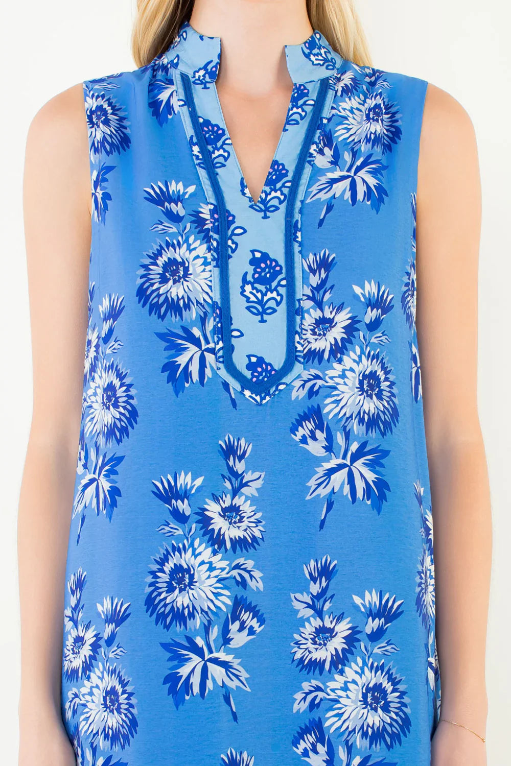 A woman wears the Zertz SLEEVELESS FLORAL PRINT DRESS with a notched neckline and decorative trim in blue and white—a stylish summer choice for any occasion.
