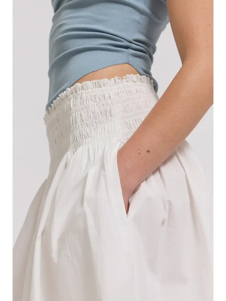 A model, shown from mid-torso to thigh, wears a light blue sleeveless top paired with the Zertz SMOCKED WAIST SKIRT in white, featuring a shirred elastic waistband and a pocket-detail on one side.
