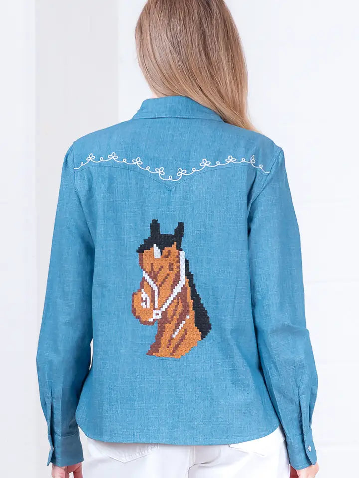A person with long, light brown hair is seen from behind wearing the Zertz DENIM EMBROIDERY TOP, featuring white decorative stitching and a large pixel art-style horse embroidery on the back.