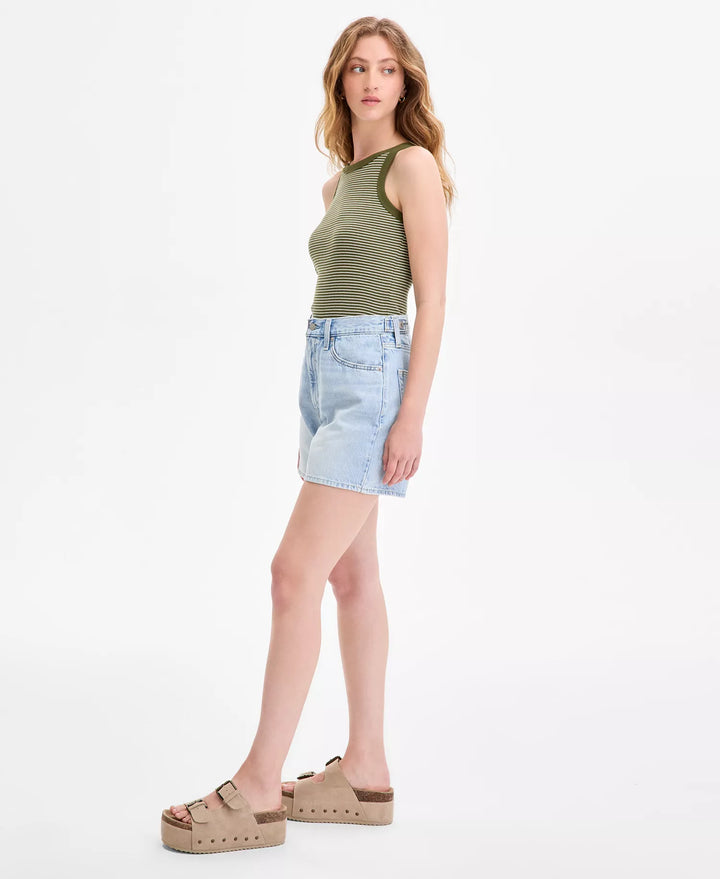 A woman stands sideways in a sleeveless green top, Zertz CINCH MID-THIGH SHORT ABRAIDED ART high-rise baggy denim shorts with an adjustable waist, and tan platform sandals against a plain white background.