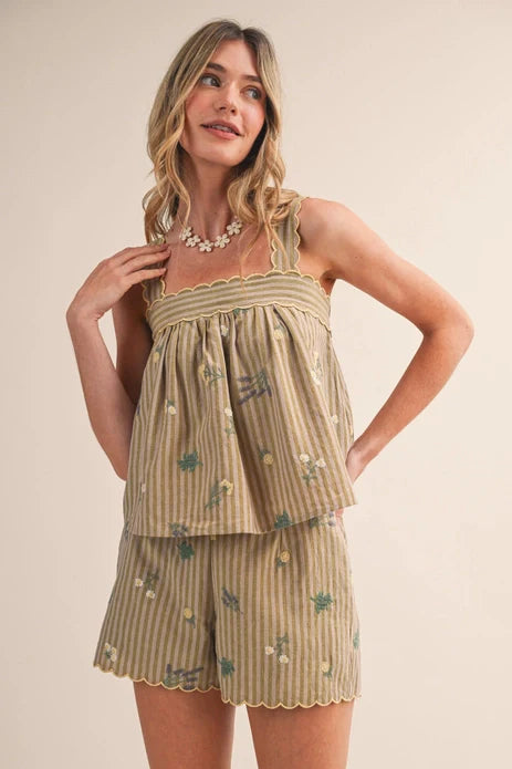 A woman smiles in the Zertz FARMERS MARKET SHORT SET MPST4474—a matching two-piece with a loose, scallop-edged tank and shorts in beige and olive green stripes with small floral prints—paired with a white flower necklace.