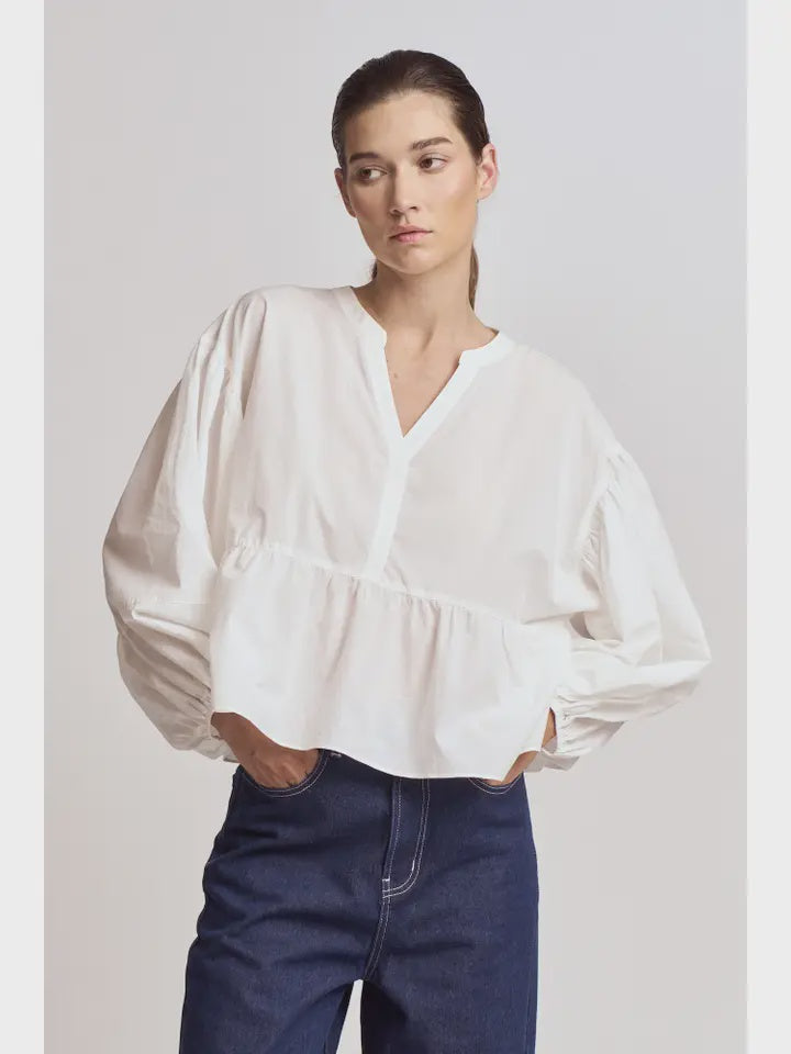 A person wears the Zertz BALOON SLEEVE BLOUSE with a romantic silhouette and dark blue high-waisted jeans, standing against a plain light background with hands in pockets for a versatile wardrobe look.
