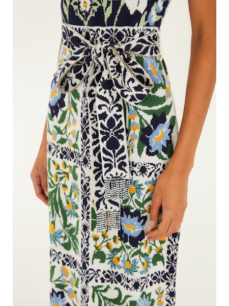 A close-up of the Zertz MANOELA KNIT MIDI DRESS, showcasing blue, green, yellow, and white floral and geometric patterns with a matching belt tied at the waist—a must-have for effortless style. A woman&
