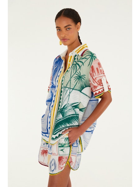 A woman models the Zertz BRASIL VINTAGE SHORTS, featuring tropical and architectural prints, paired with a matching shirt. She stands against a white background, hand in her pocket, gazing slightly to the side.