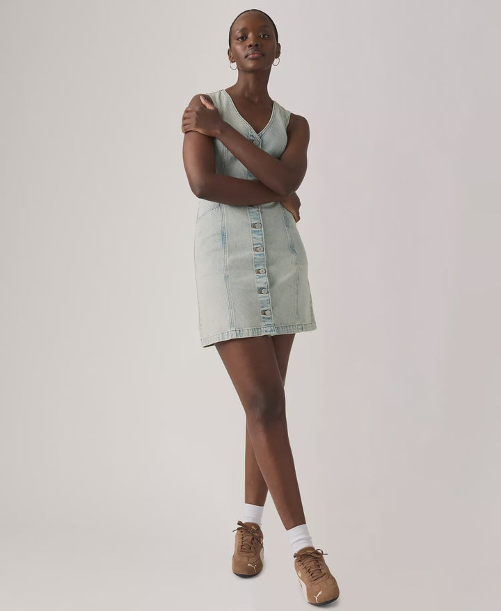 A person stands with arms crossed, wearing the Zertz VIANNA VEST DRESS- A LITTLE HAZY DRESS, paired with white socks and brown sneakers, against a plain light background.