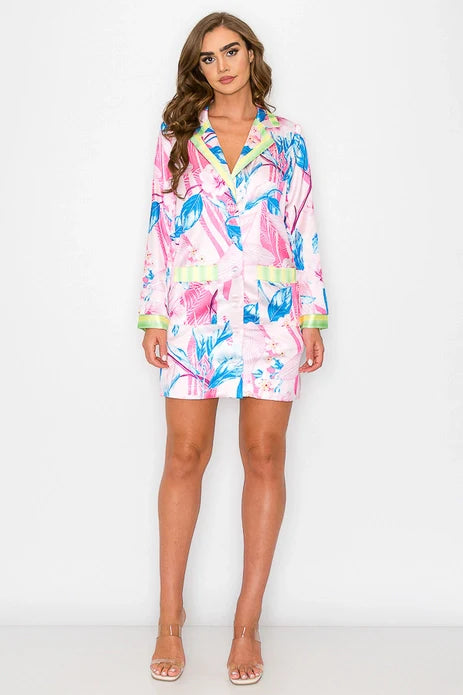 A woman with long wavy hair poses against a white background wearing the Zertz FLORAL PRINTED SHIRT DRESS, featuring blue and green tropical leaf patterns and paired with nude heels.