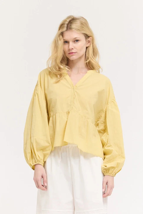 A woman with blonde hair models the Zertz BALOON SLEEVE BLOUSE in yellow, featuring a romantic silhouette and v-neck, styled with white wide-leg pants against a light background for an effortlessly chic look.