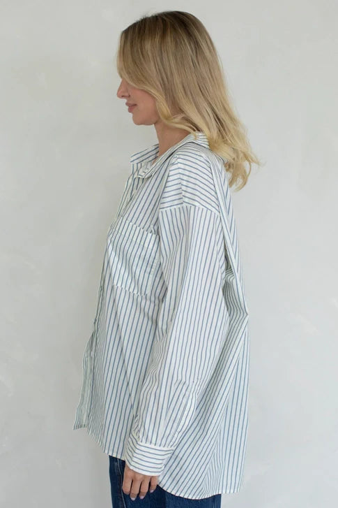 A blonde woman in profile models the Zertz STRIPED OVER SIZED BUTTON UP TOP—a classic, long-sleeved striped shirt—against a plain light background.