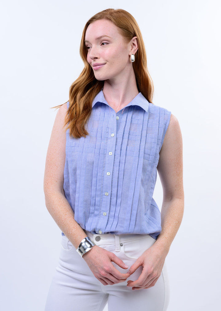 A woman with long red hair models the Zertz TUCKED PATTERN SHIRT, a sleeveless light blue casual top, paired with white pants. She completes the look with silver hoop earrings and a cuff bracelet against a plain white background.