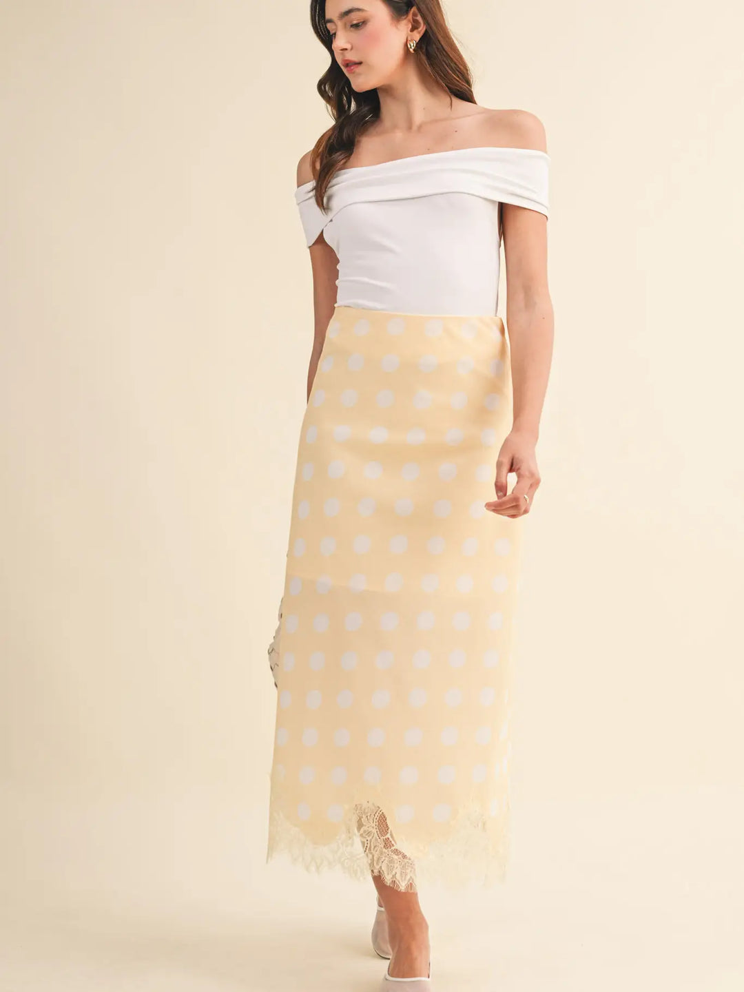 A woman stands against a plain beige background wearing the Zertz POLKA DOT LACE TRIM SKIRT and an off-the-shoulder white top.