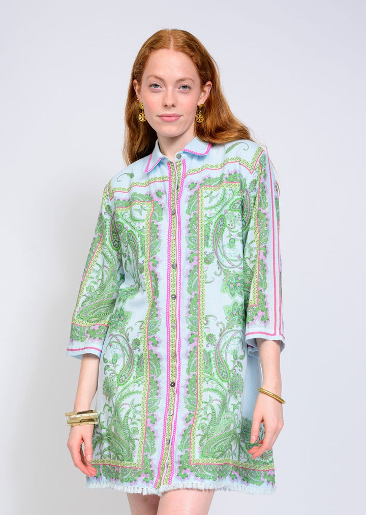 A woman with long red hair wears the Zertz PAISLEY SHIFT DRESS, a green paisley print button-up with pink borders and a relaxed silhouette, styled with gold hoop earrings and bracelets against a plain light background.