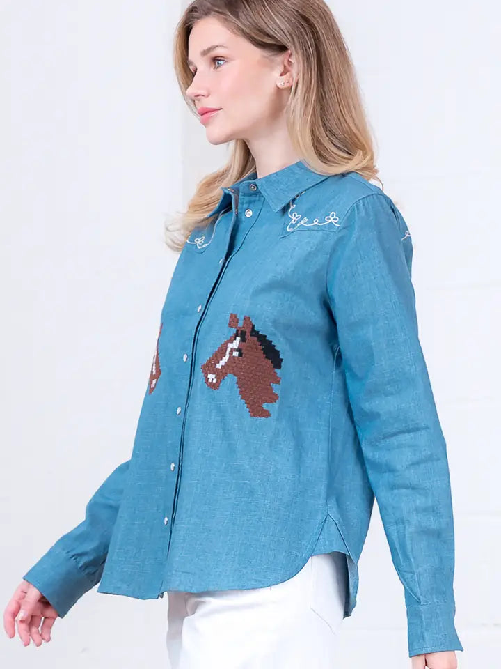 A woman with light brown hair models the Zertz DENIM EMBROIDERY TOP, featuring horse embroidery, paired with white pants. She stands sideways against a light background.