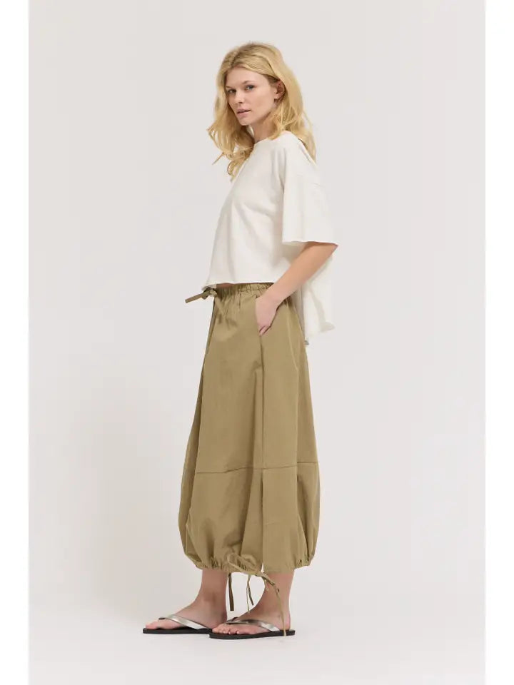 A woman with light wavy hair stands sideways against a plain background, wearing the Zertz LOOSE LONG SLEEVE TEE, tan drawstring wide-leg pants with cinched ankles, and white sandals. She has a neutral expression.