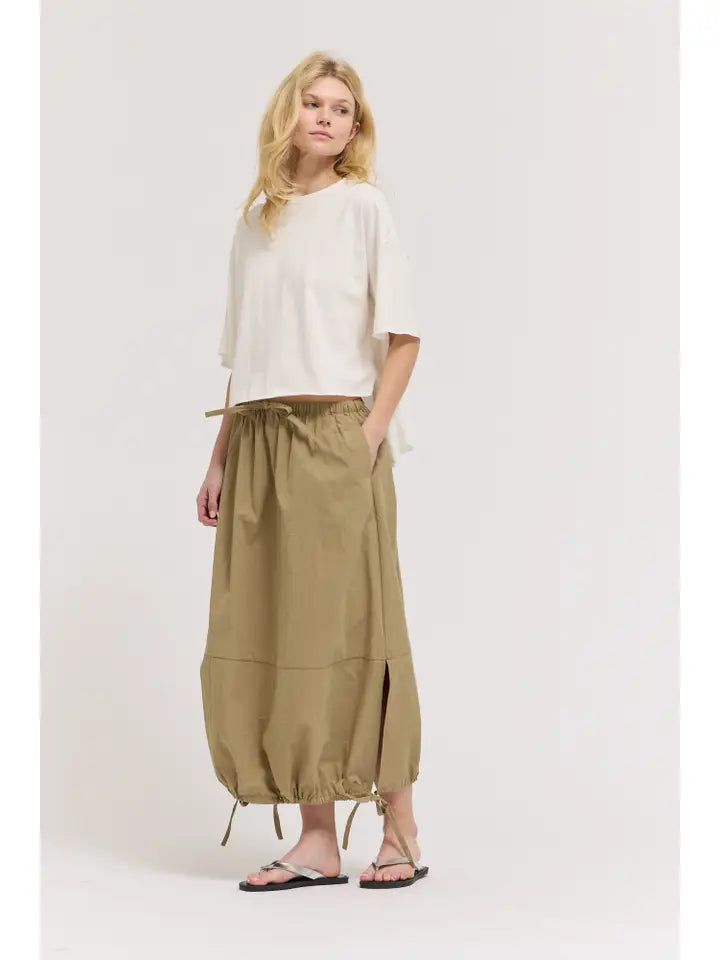 A person with light hair and a relaxed expression stands against a plain background wearing the Zertz LOOSE LONG SLEEVE TEE, an olive green drawstring maxi skirt with side slits, and black flip-flops.
