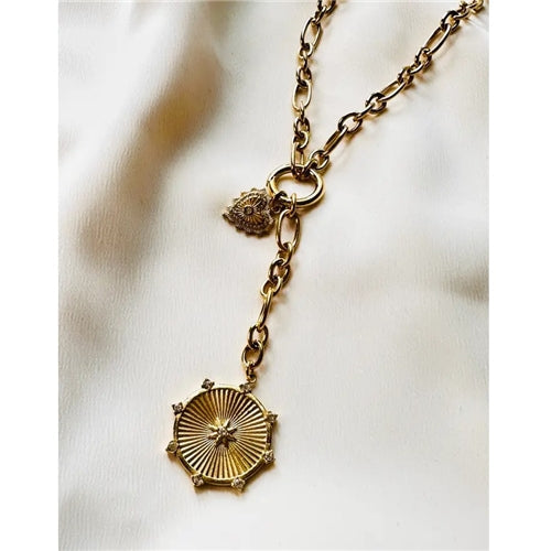 The Circle the Stars Necklace by Loca on Main features a chunky chain with an intricate sunburst hexagonal pendant and a small circle star charm, displayed on a cream fabric background.