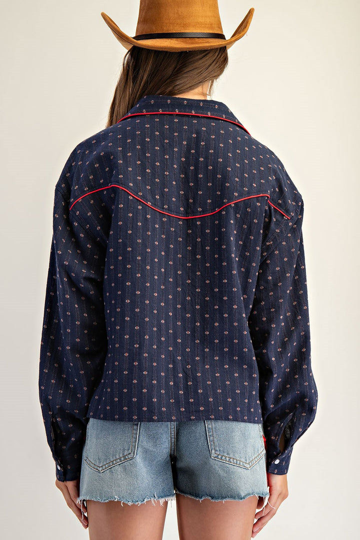 A person is seen from the back wearing Zertz’s WESTERN BUTTON DOWN SHIRT—blue with red piping and embroidered patterns—paired with a brown cowboy hat and light denim shorts, standing against a neutral background.