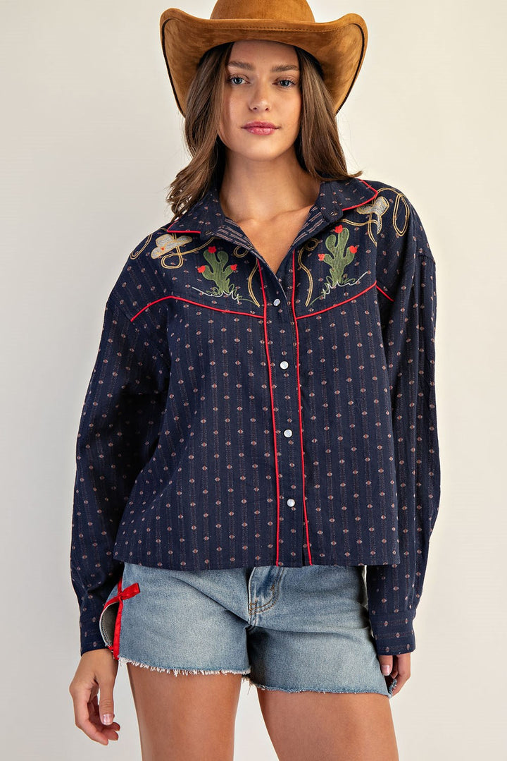 Woman in a brown cowboy hat, Zertz WESTERN BUTTON DOWN SHIRTS with cacti and rope embroidery, and light blue denim shorts, standing against a plain light background.