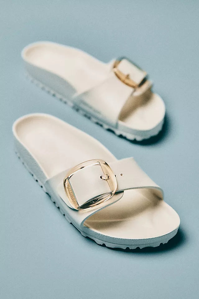 The Zertz MADRID BB EVA EGGSHELL are ultra-lightweight white slide sandals with thick soles and wide straps, each featuring a large shiny gold buckle. Stylish and water-resistant, they&