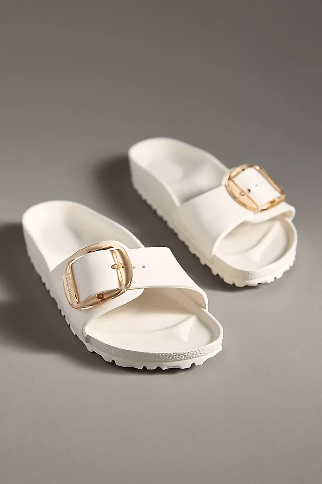 The Zertz MADRID BB EVA EGGSHELL sandals are ultra-lightweight white slides with thick soles and large gold buckles, displayed on a neutral gray surface.