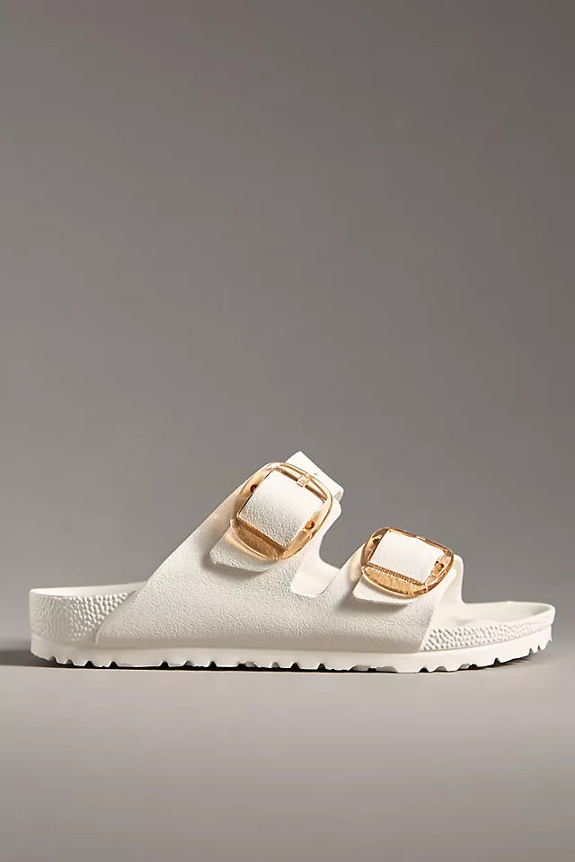 The Zertz ARIZONA BB EVA EGGSHELL N is a white EVA sandal with two wide straps, each with a large gold buckle. It features an ultra-lightweight, textured BIRKENSTOCK footbed and flat sole, set against a plain gray background.