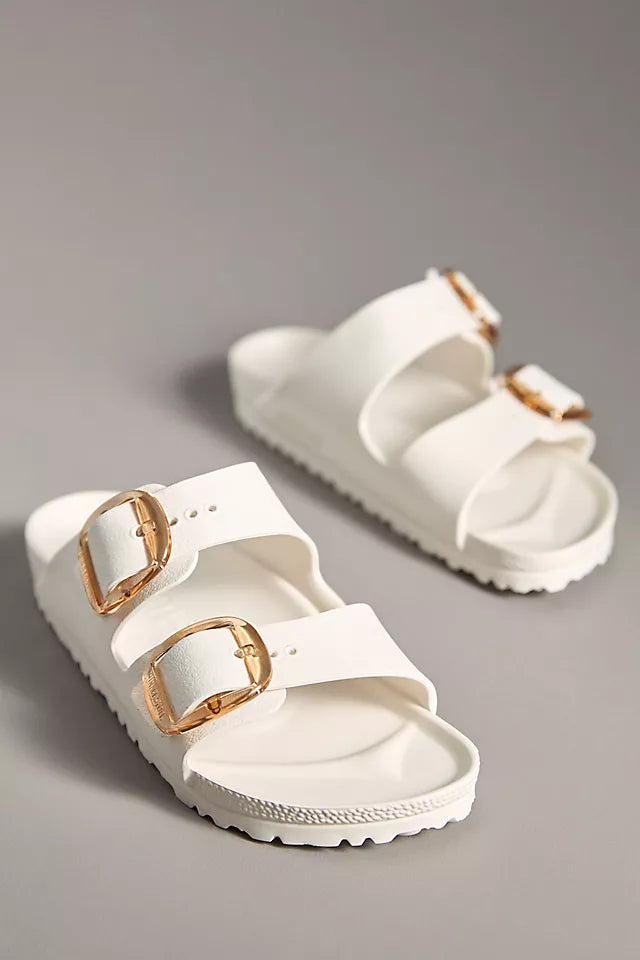 The Zertz ARIZONA BB EVA EGGSHELL N sandals are ultra-lightweight white slides with two wide straps, large gold buckles, and a comfy footbed, shown on a neutral gray background.