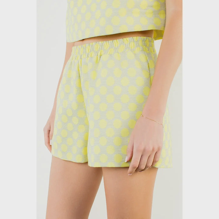 A person wears Zertz POLKA DOT SHORTS with a matching sleeveless crop top featuring an elastic waistband. This lightweight set offers a casual, breezy style ideal for warm days.