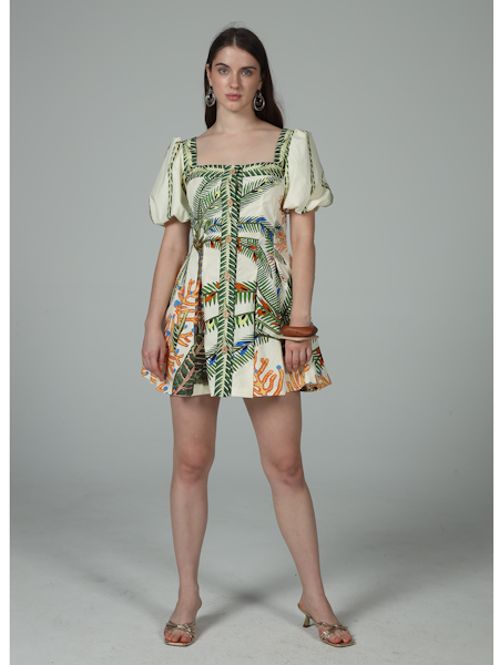 A woman faces the camera in the Zertz CORA PUFF MINI DRESS, featuring vibrant tropical leaf and animal prints—an ideal vacation look—styled with hoop earrings, bangles, and open-toe heels against a plain gray background.