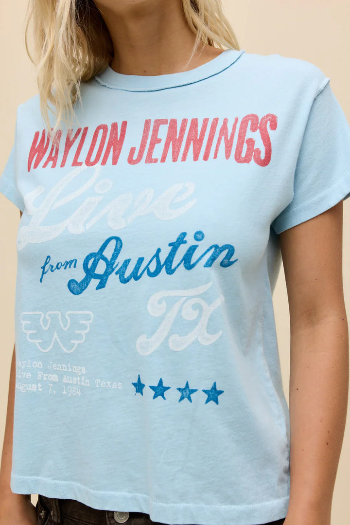 A woman wears the Zertz WAYLON JENNINGS LIVE FROM ATX REVERSE GF TEE—a light blue shirt with stars, Flying W logo, and "Live from Austin TX" text. The image is cropped neck to waist.