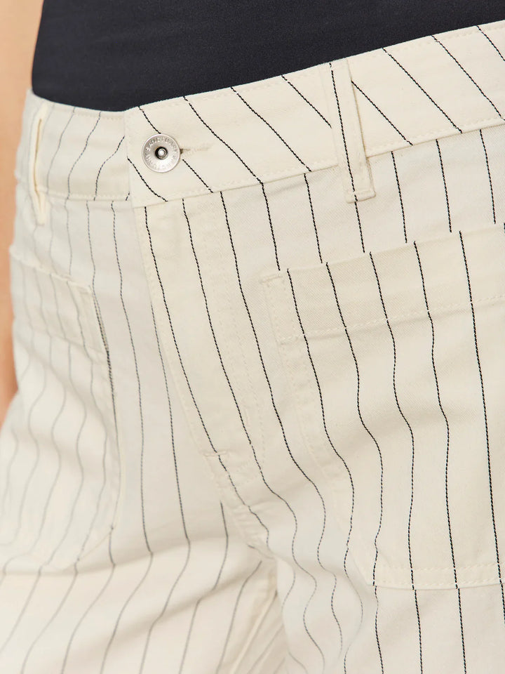 Close-up of a person wearing THE MARINE PANT by Zertz—off-white pinstripe, cropped wide leg pants with front pockets, silver button waistband—paired with a dark top.