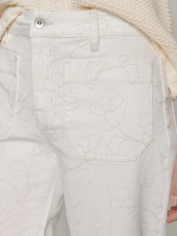 Close-up of a person wearing THE MARINE CROP by Zertz—off-white, relaxed fit, cropped wide leg jeans with floral embroidery. Focus is on the back pocket and hip area, paired with a cream textured sweater.