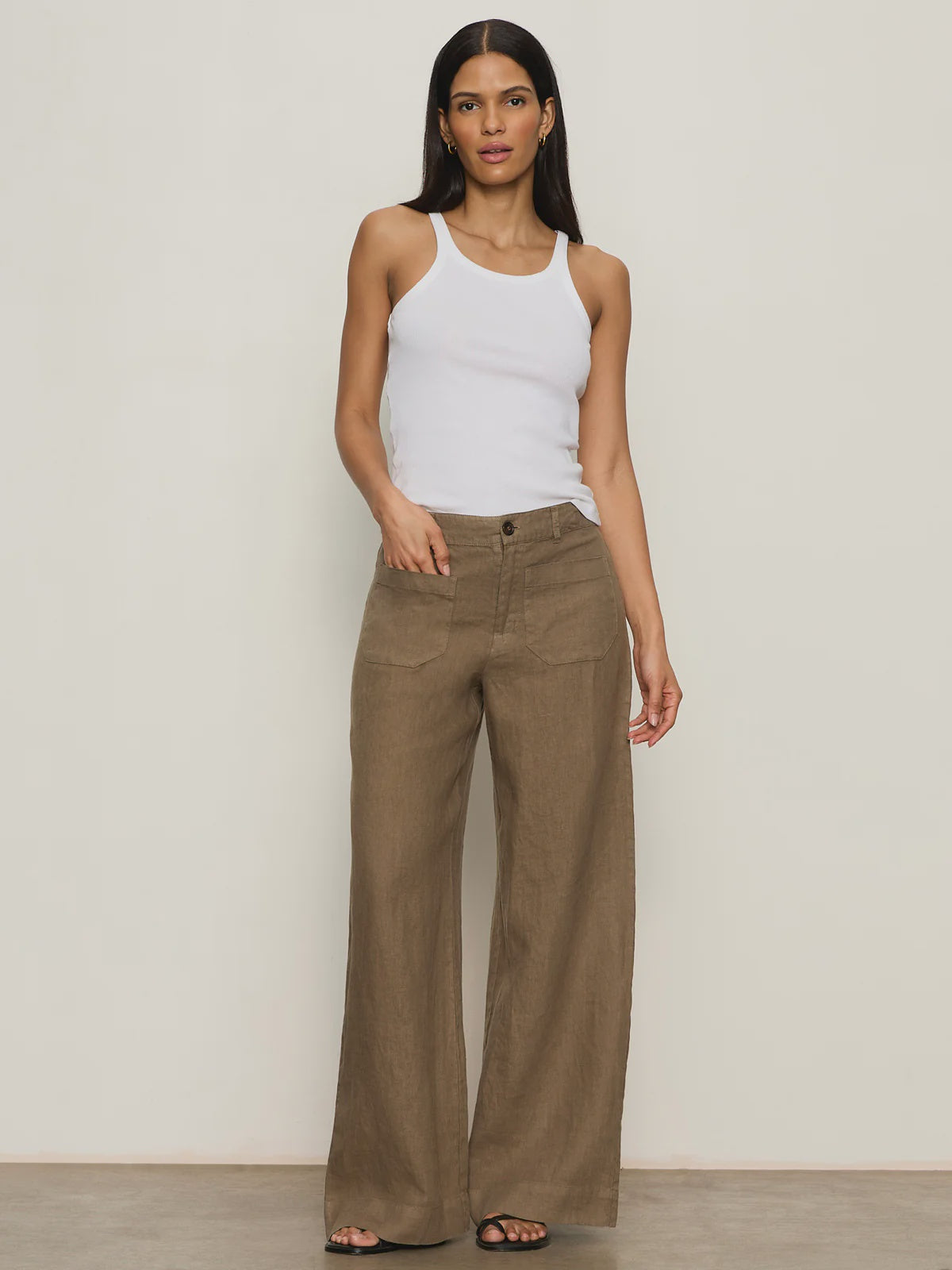 A woman stands against a plain background wearing Zertz's THE LINEN MARINE WIDE LEG PANT CP1043716 in brown, paired with a white sleeveless tank top and black sandals. She has straight, dark hair and a neutral expression.