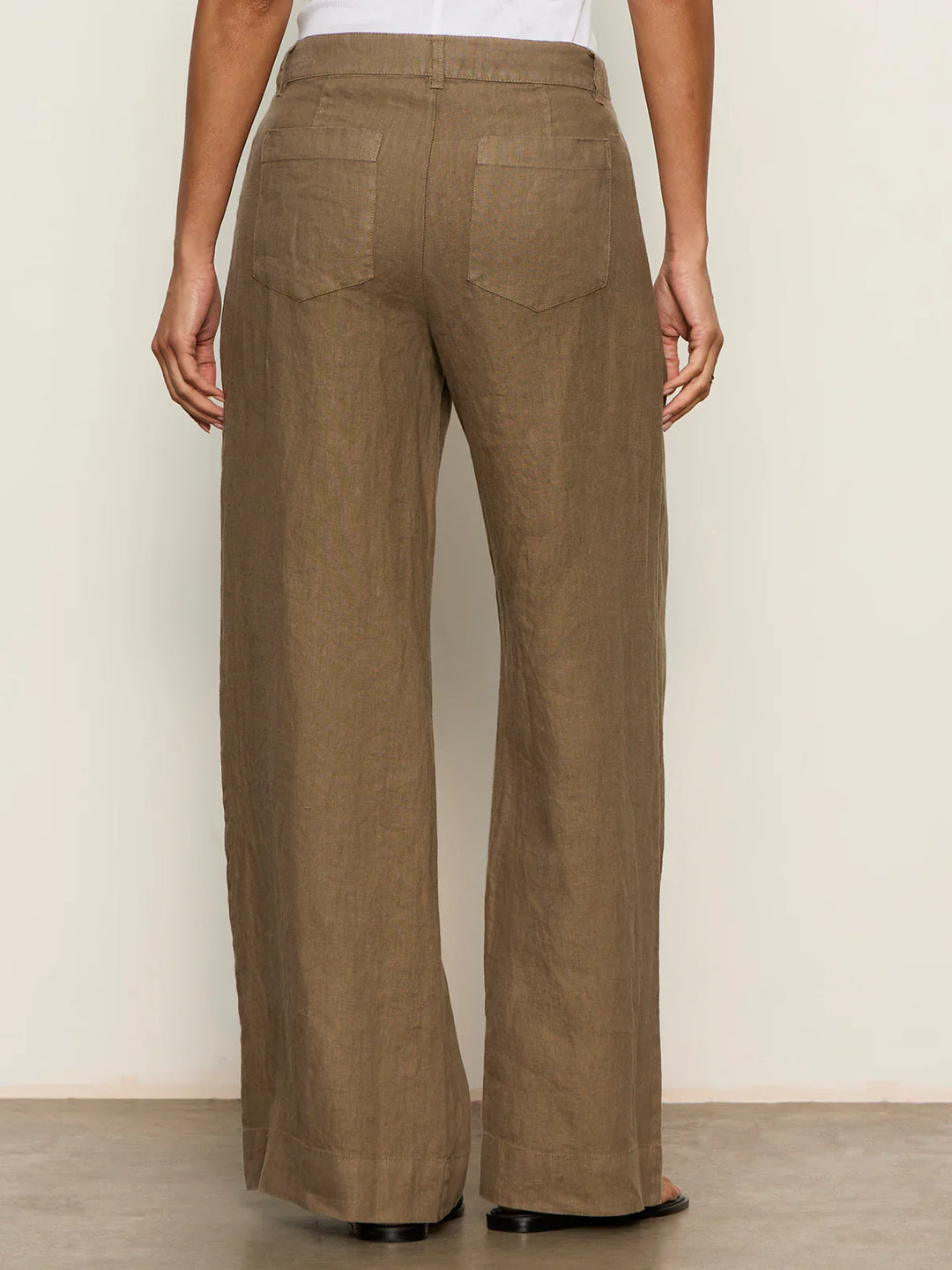 A person is seen from behind wearing Zertz’s THE LINEN MARINE WIDE LEG PANT CP1043716, a high-waisted, wide-leg brown pant with back pockets, standing against a plain light wall.