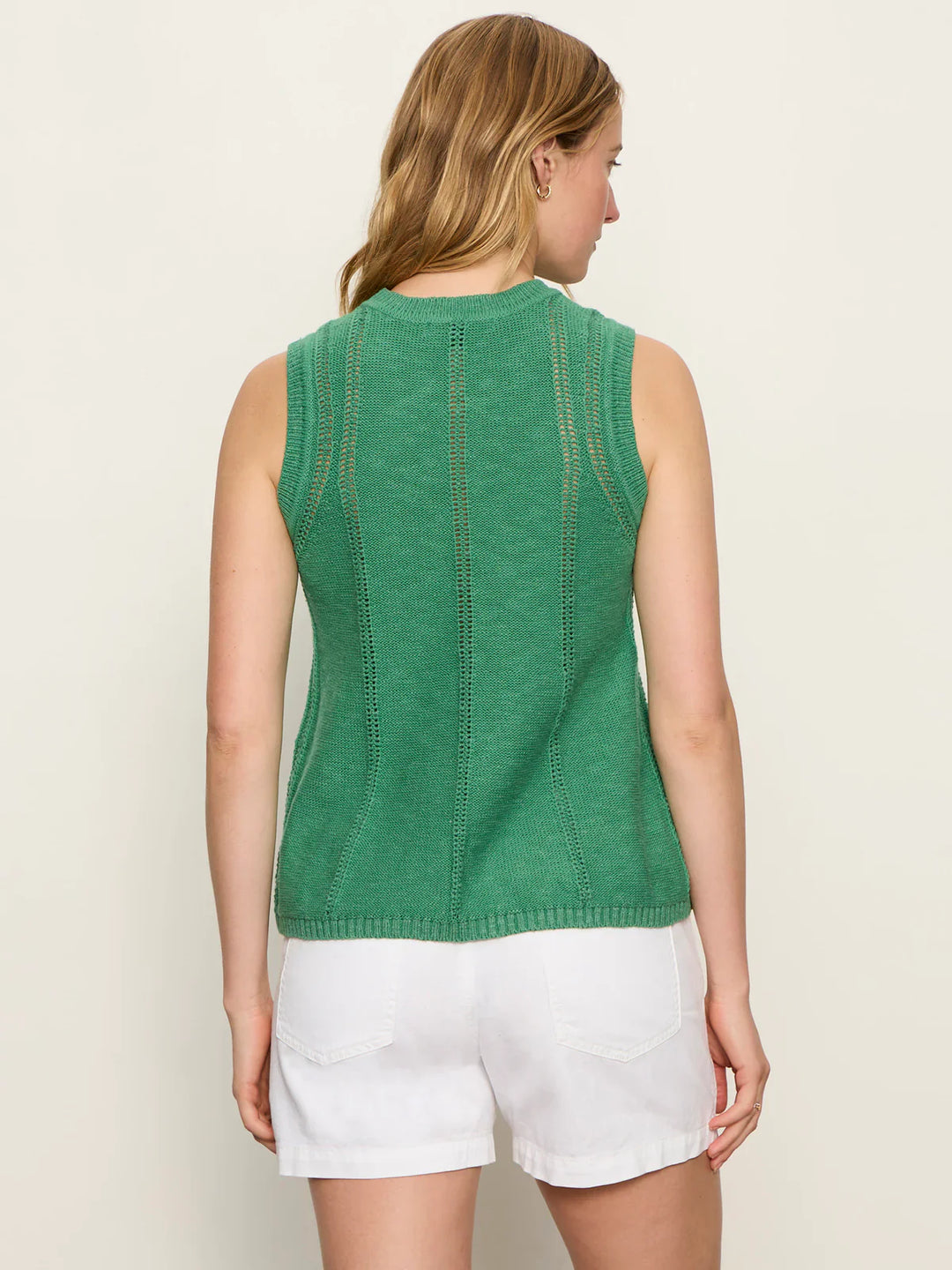 A woman with light brown hair faces away, wearing the Zertz EASY POINTELLE SHELL sleeveless green knit top and white shorts against a plain light background.