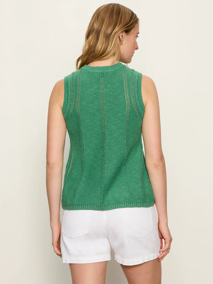 A woman with light brown hair faces away, wearing the Zertz EASY POINTELLE SHELL sleeveless green knit top and white shorts against a plain light background.