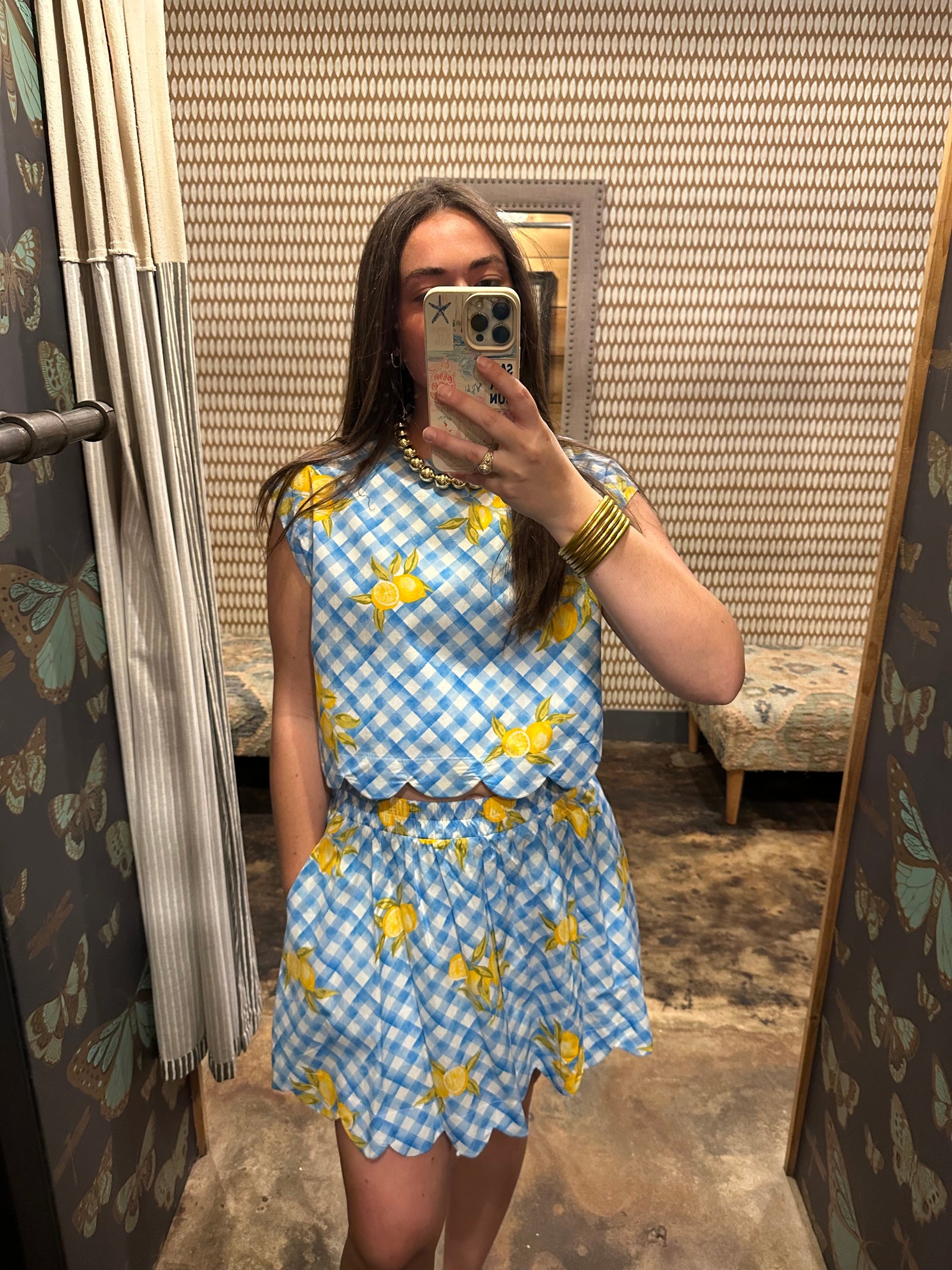 A woman stands in a fitting room taking a mirror selfie, wearing the Zertz 2 PIECE LEMON SET. Her playful look complements the butterfly wallpaper and patterned walls.