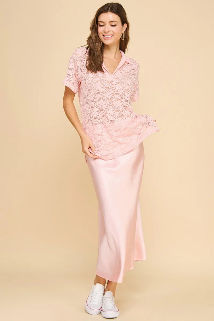 A woman poses against a beige backdrop, smiling in the Zertz ANISTON SATIN SLIP SKIRT paired with a light pink lace top and white sneakers, showing off its versatile style with one hand on her hip and the other holding her shirt.