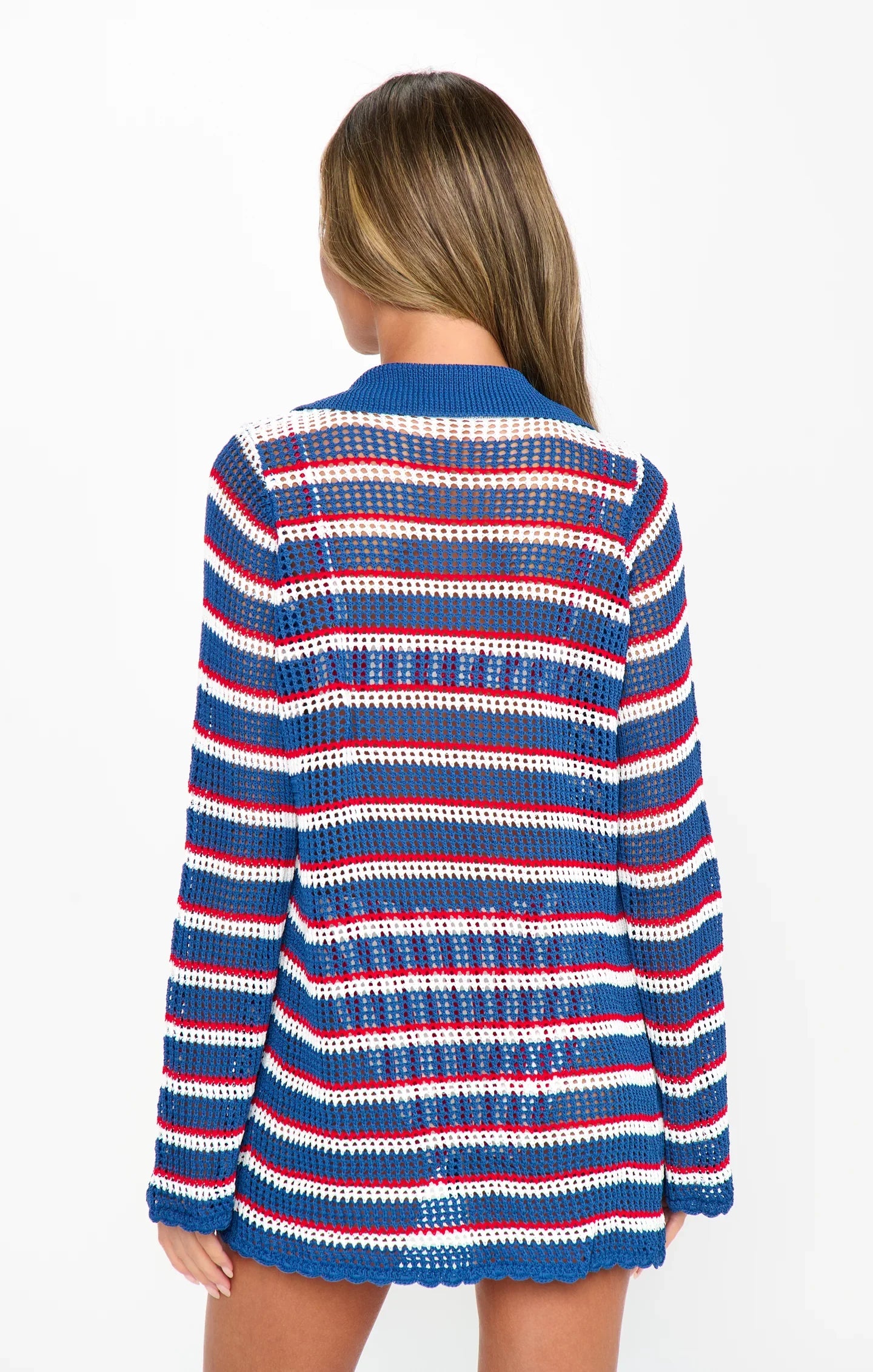 A woman with long hair stands facing away, wearing the Zertz BUTTON UP COVERUP—a long-sleeve, open-knit striped sweater in blue, red, and white—perfect for your summer wardrobe. The background is plain white.