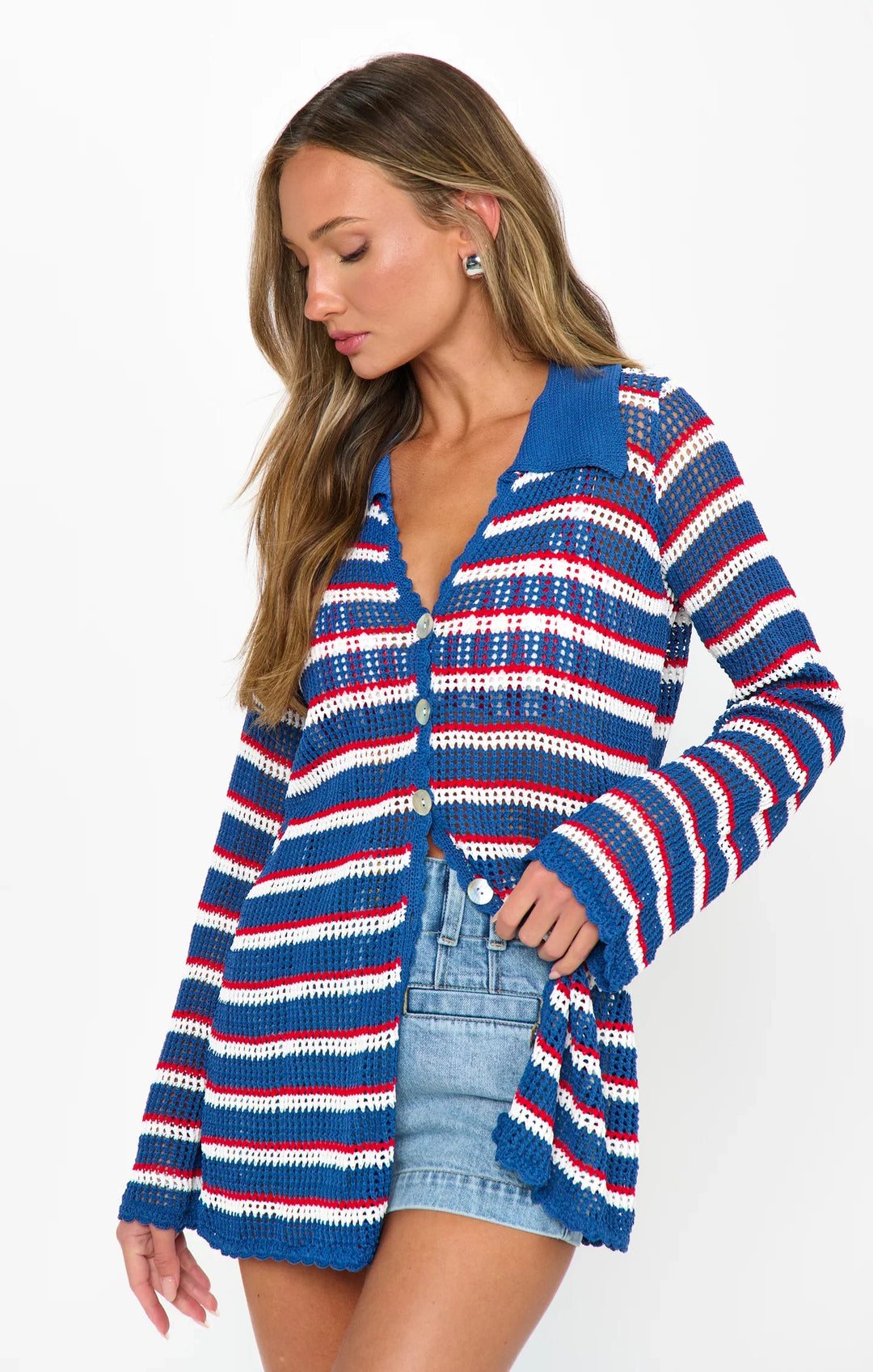 A woman with long hair models the Zertz BUTTON UP COVERUP—featuring blue, red, and white stripes—over a blue tank top and denim shorts, perfect for summer style, posing against a white background.