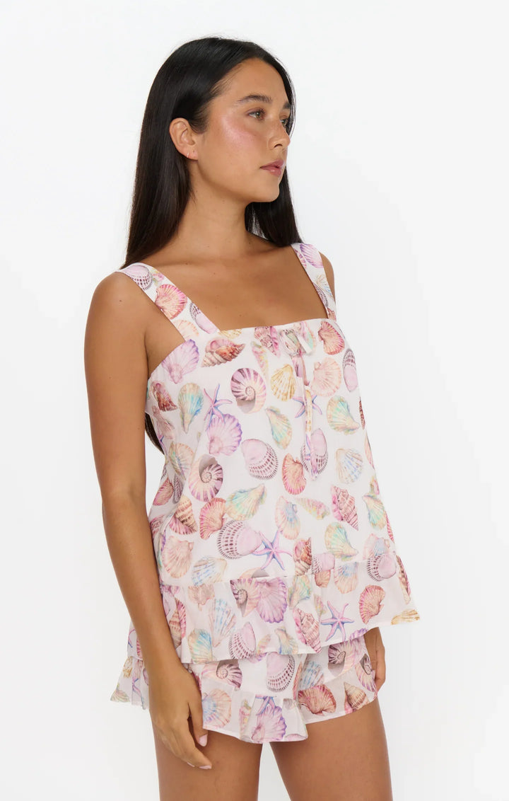 A woman models the Zertz LAYLA SET—sleeveless tie-front top and matching shorts with a seashell and starfish print—against a white backdrop, making it the ideal playful vacation outfit.