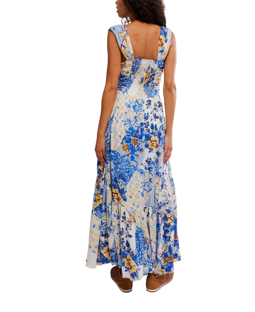 A woman faces away in the Zertz SASHA MAXI, a blue, yellow, and white patchwork floral dress with wide straps and a square back. She pairs this elegant maxi dress with brown sandals.